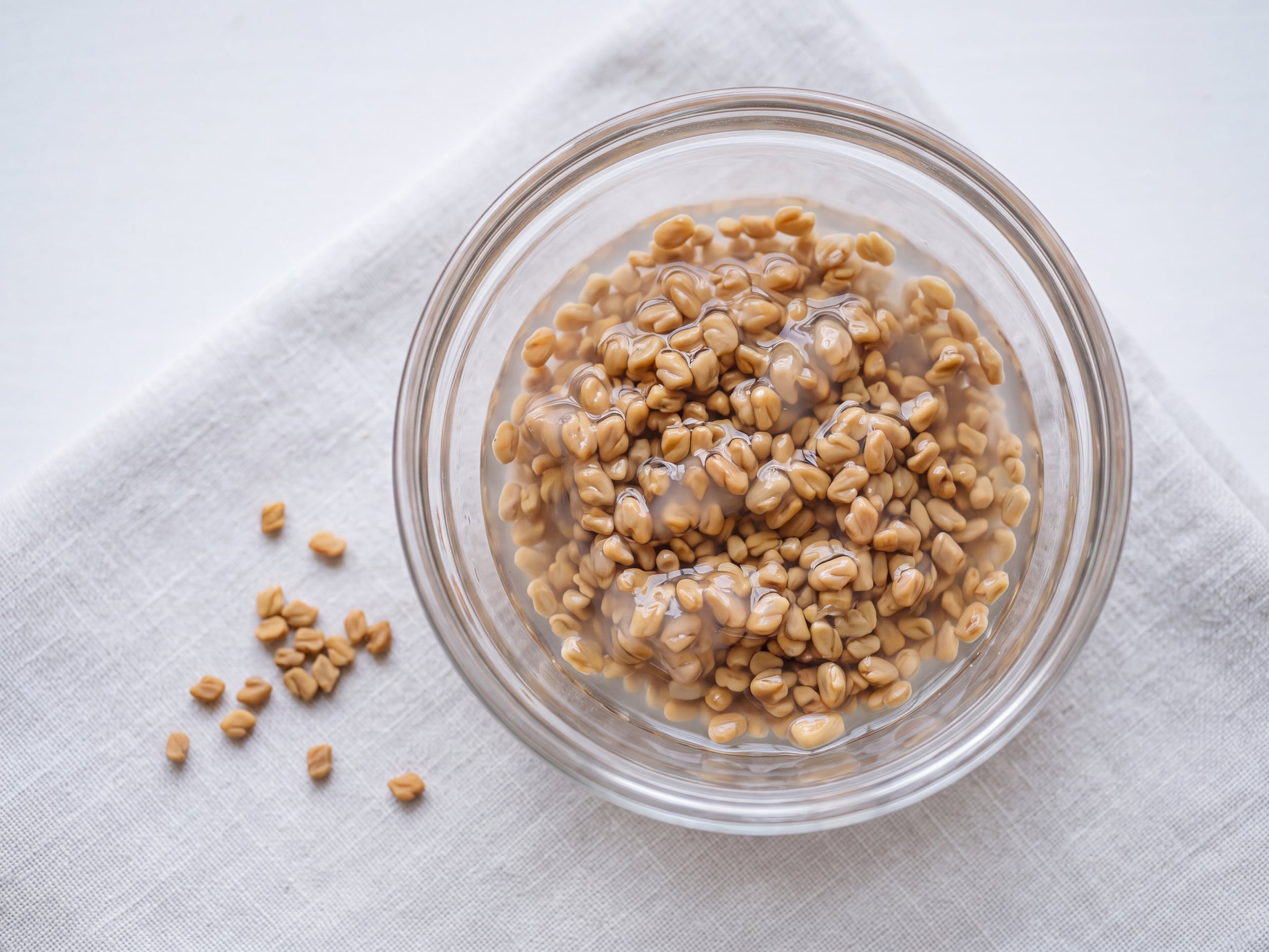 Fenugreek seeds soaking in a glass bowl of water showing the translucent mucilage gel coating