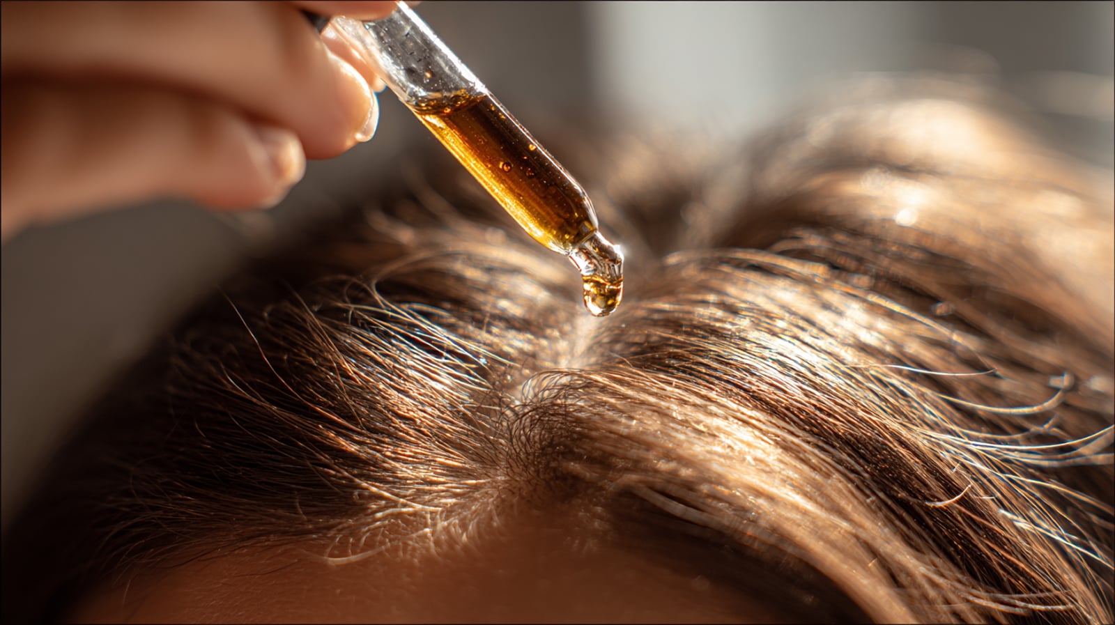 A glass dropper applying moringa oil directly to a clean scalp to moisturize and support hair health.