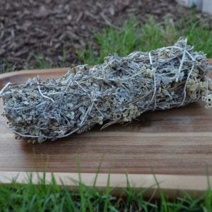 A natural, dried Imphepho (African Sage) smudge stick resting in a wooden bowl outdoors, highlighting its herbal origin.
