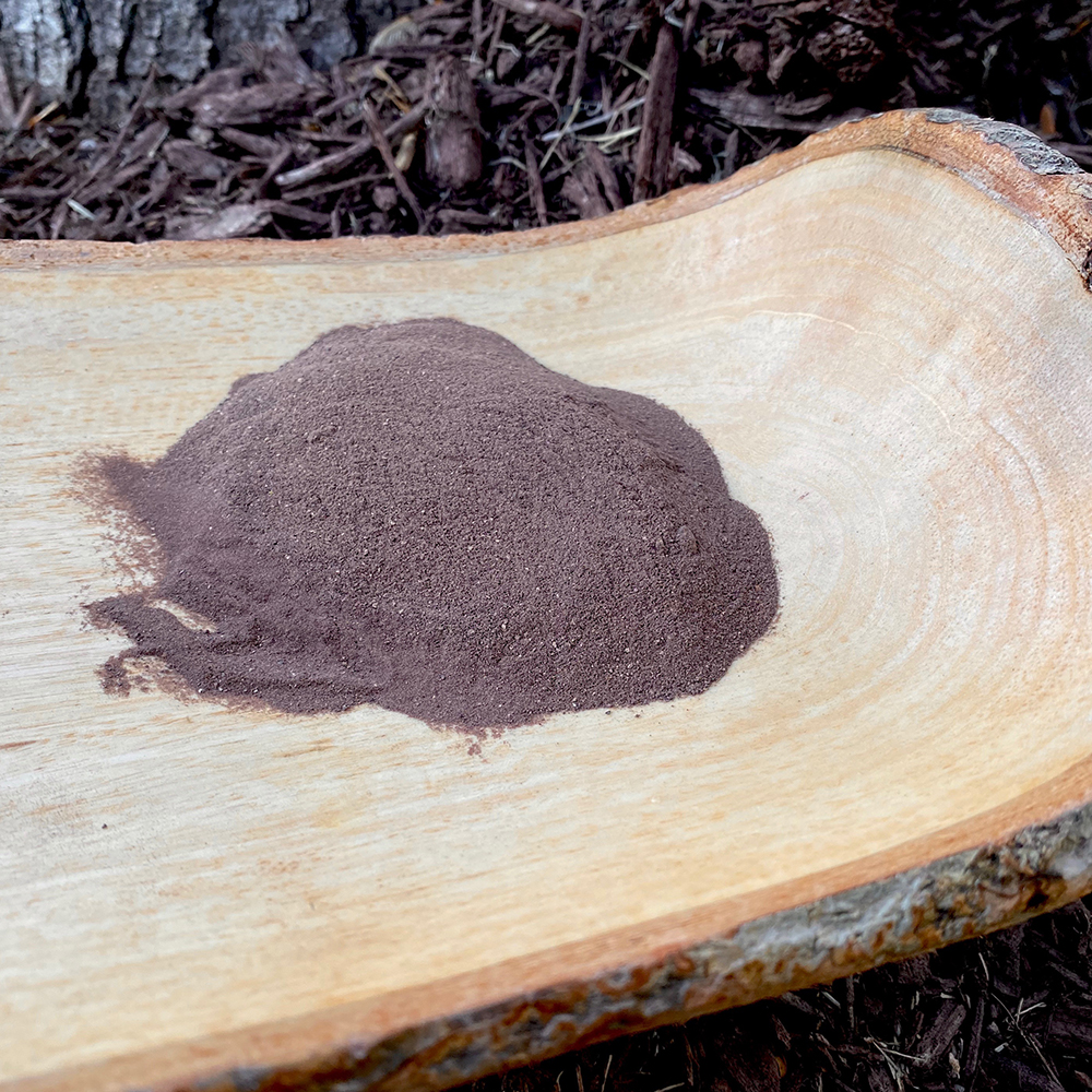 Black Ginger Powder A mound of fine, dark purple black ginger powder displayed on a natural wood slice, showing its rich color and texture.