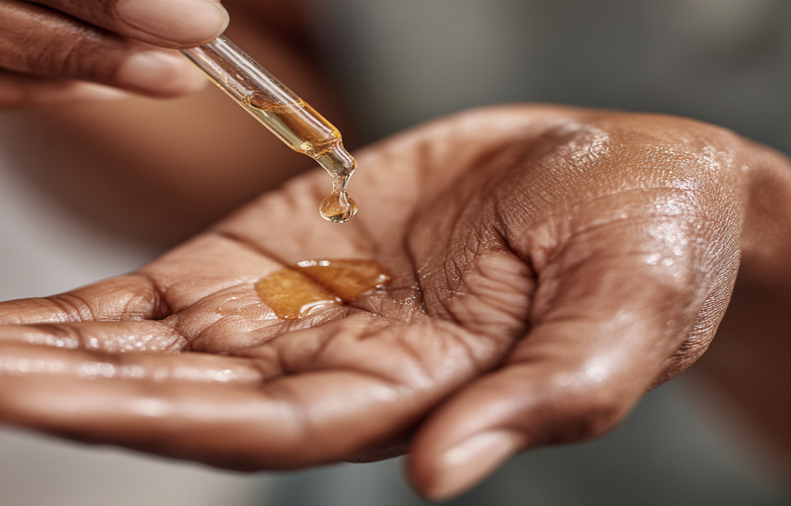 A person applying a single drop of high-linoleic safflower oil to their skin as a natural moisturizer.
