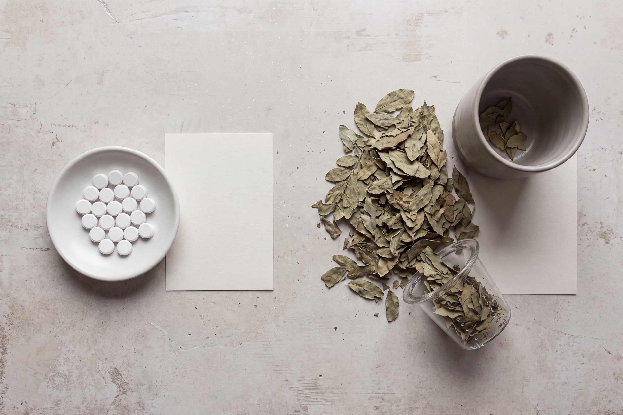 Measured senna tablets in a ceramic dish beside loose senna leaf tea with a glass infuser and cup