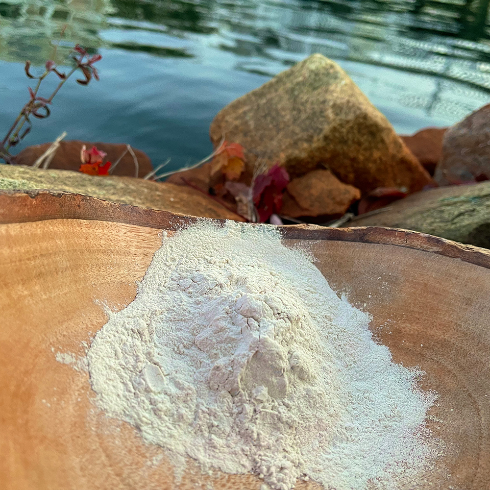 Sea Moss Powder A wooden bowl of fine, organic Irish sea moss powder sitting on rocks next to clean, natural water, illustrating its pure, wildcrafted source.